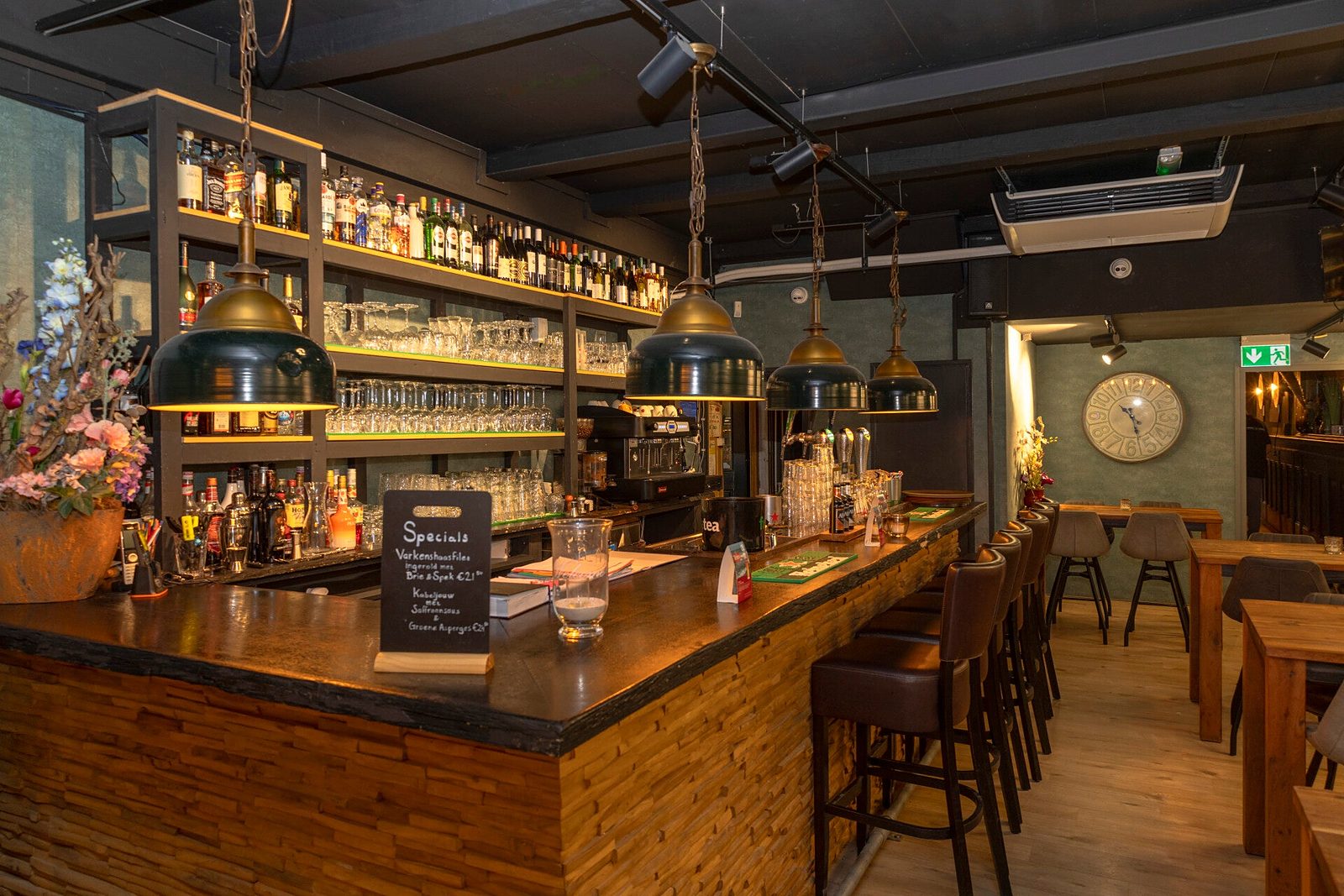 De bar van Steakhouse de Moriaan met koperen lampen, houten bar en een volle flessenwand